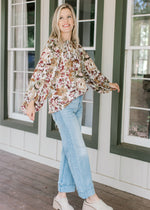 Model wearing jeans, mules and a cream top with warm fall floral, high neck ruffle and long sleeves.