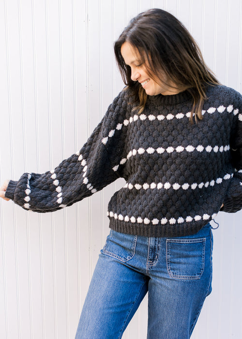 Model wearing a black textured sweater with white striped dots and bubble long sleeves.