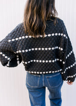 Back view of Model wearing a black sweater with white dots and bubble long sleeves.