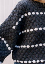 Close up of texturing on a black sweater with white dots in a line and long sleeves.