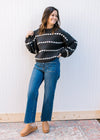 Model wearing jeans, clogs and a black sweater with white striped dots and long sleeves.