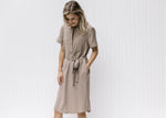 Model wearing a taupe knee length dress with a hidden front zipper, tie at waist and short sleeves. 