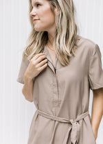 Close up of short sleeves, v-neck and tie at the waist of a taupe knee length dress. 
