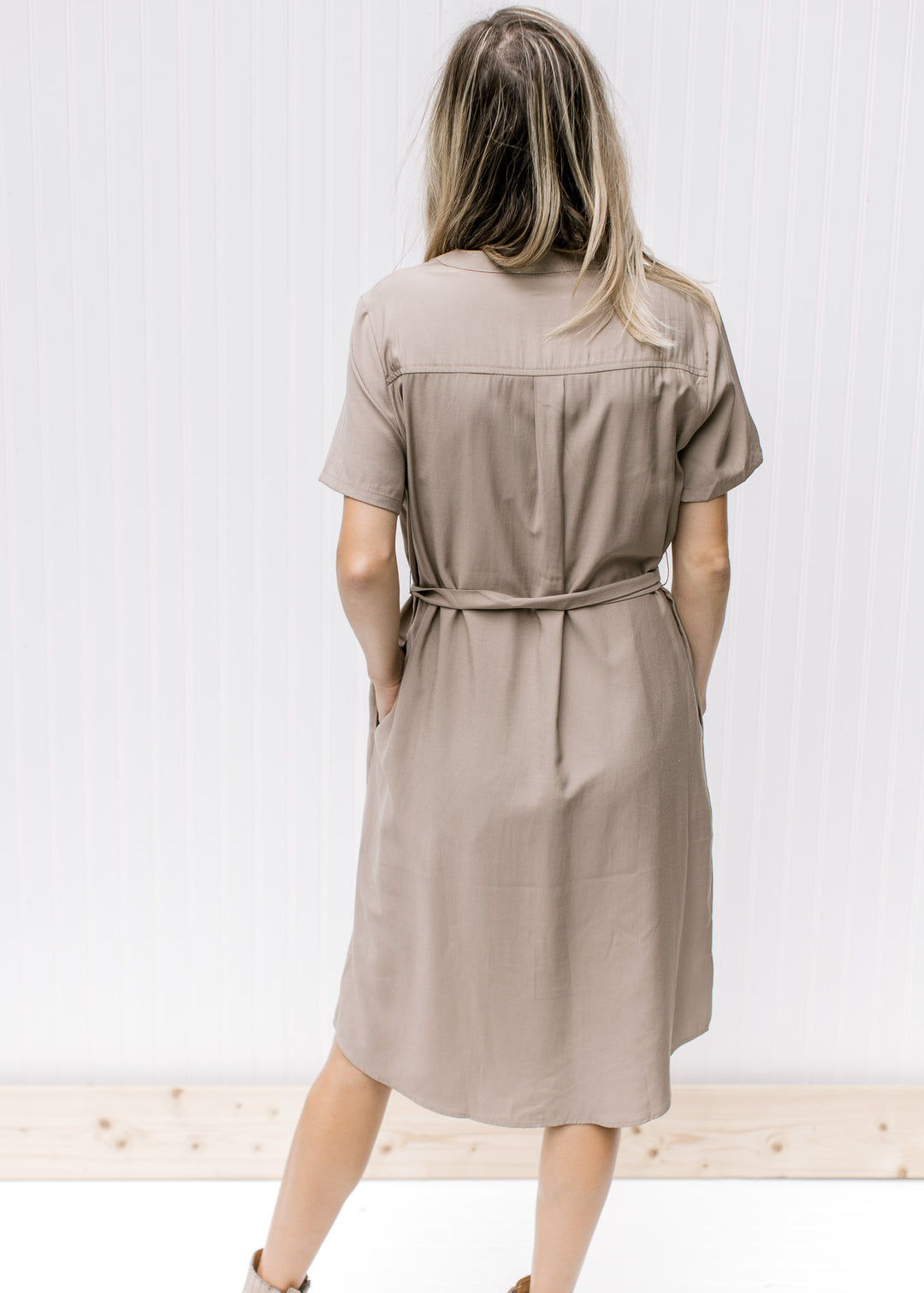 Back view of Model wearing a taupe knee length dress with a hidden front zipper and short sleeves.