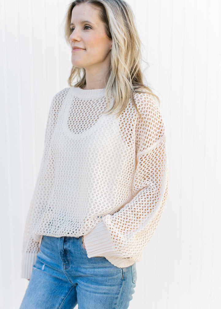 Model wearing jeans with a cream open weave sweater with a round neck and long sleeves.