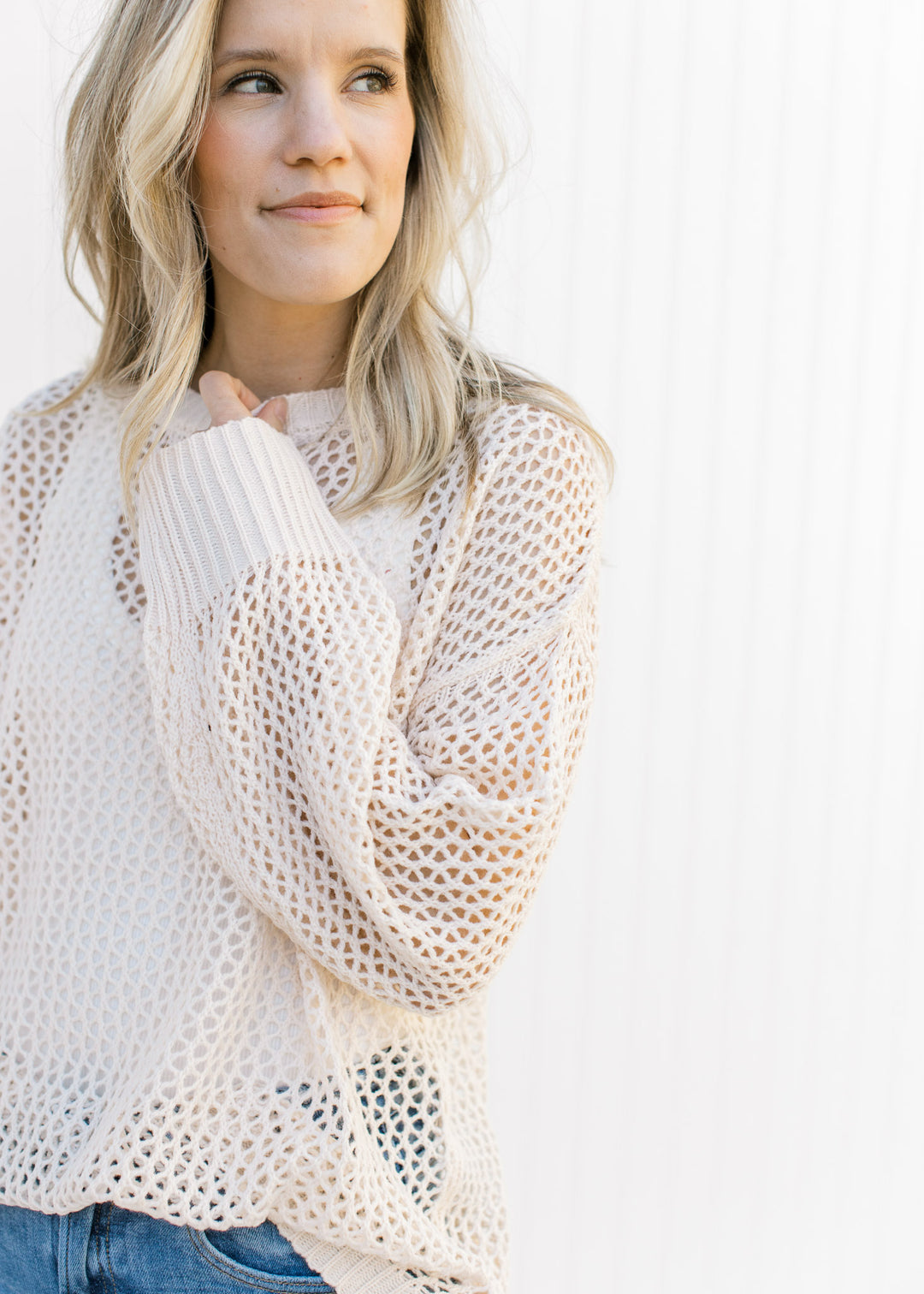 Model wearing a cream open weave sweater with a round neck and long sleeves. 