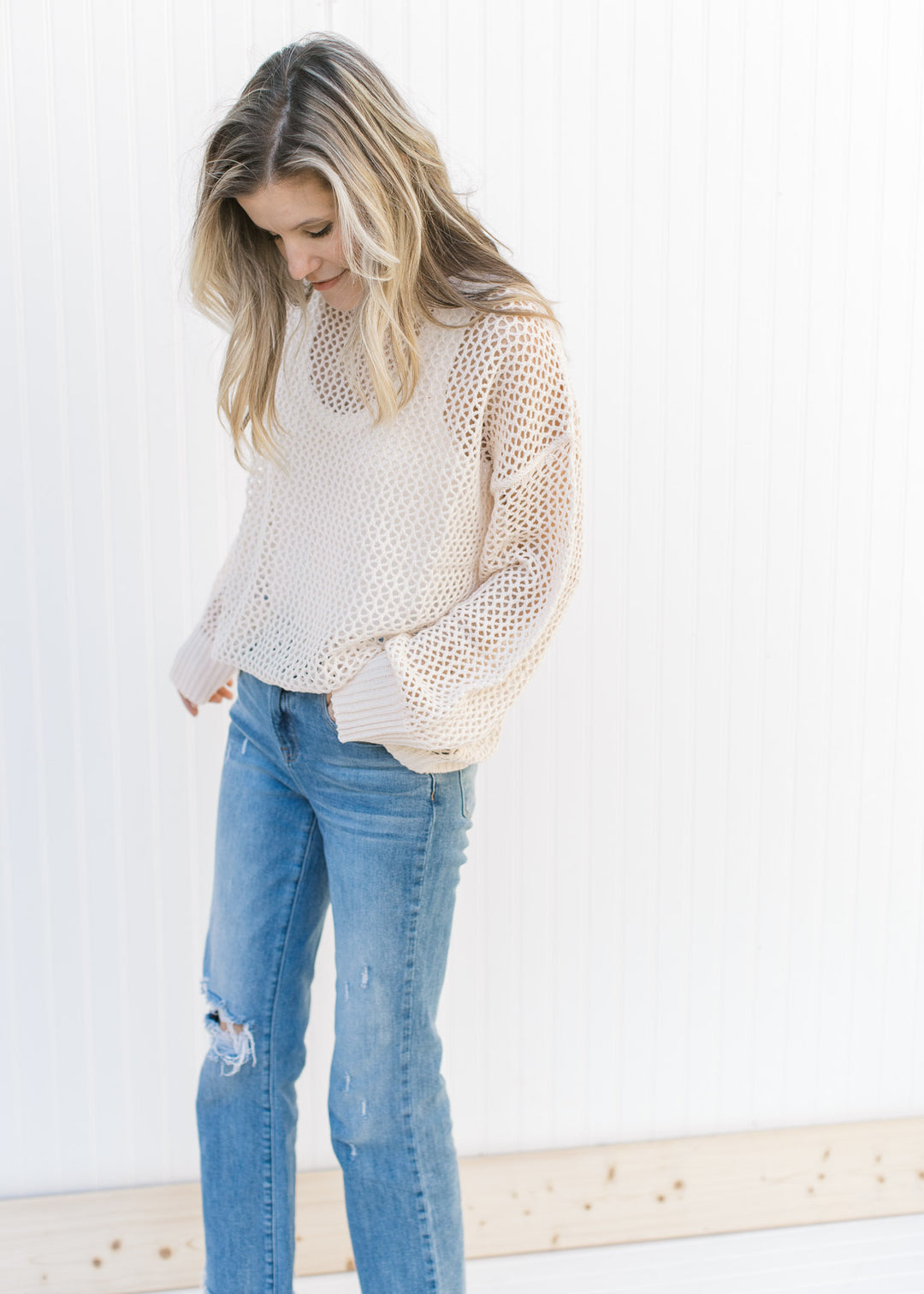 Model wearing a white take under a cream open weave sweater with long sleeves.