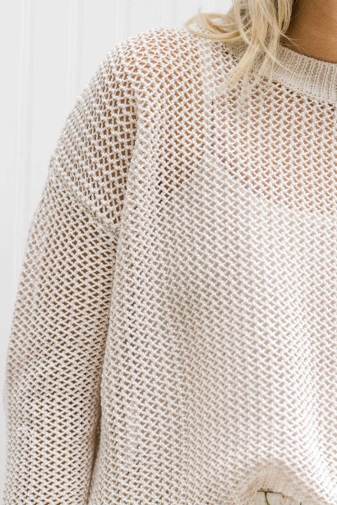 Close up view of Model wearing a cream open weave sweater with long sleeves and a round neck.
