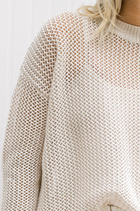 Close up view of Model wearing a cream open weave sweater with long sleeves and a round neck.
