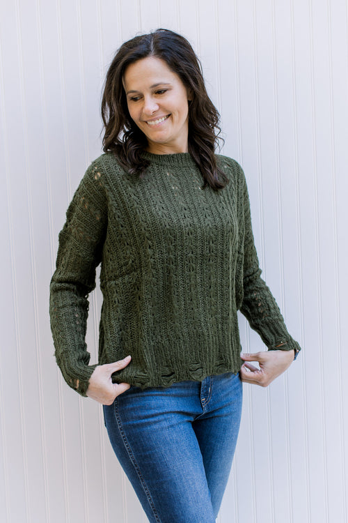 Model wearing an olive cable knit sweater with a distressed hem and cuff with long sleeves. 