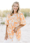 Model wearing a orange top with a neutral floral patter, short puff sleeves and a babydoll fit. 