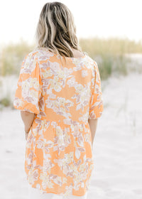 Back view of Model in an orange top with a neutral floral patter, short sleeves and a babydoll fit. 