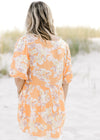 Back view of Model in an orange top with a neutral floral patter, short sleeves and a babydoll fit. 