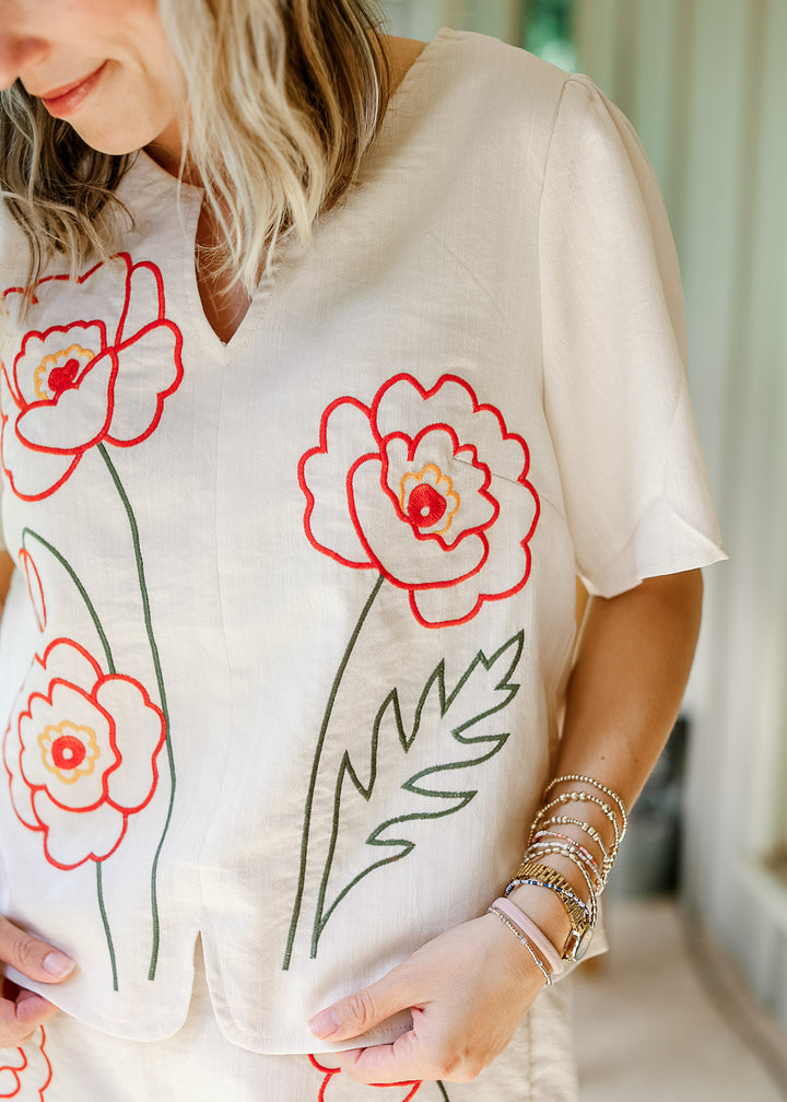 Model wearing a cream set with orange embroidered floral, v-neck and short sleeve top. 