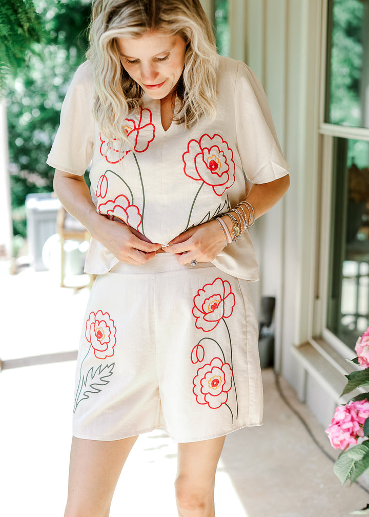 Model wearing a cream set with orange floral, short sleeve, v-neck top and shorts with pockets. 