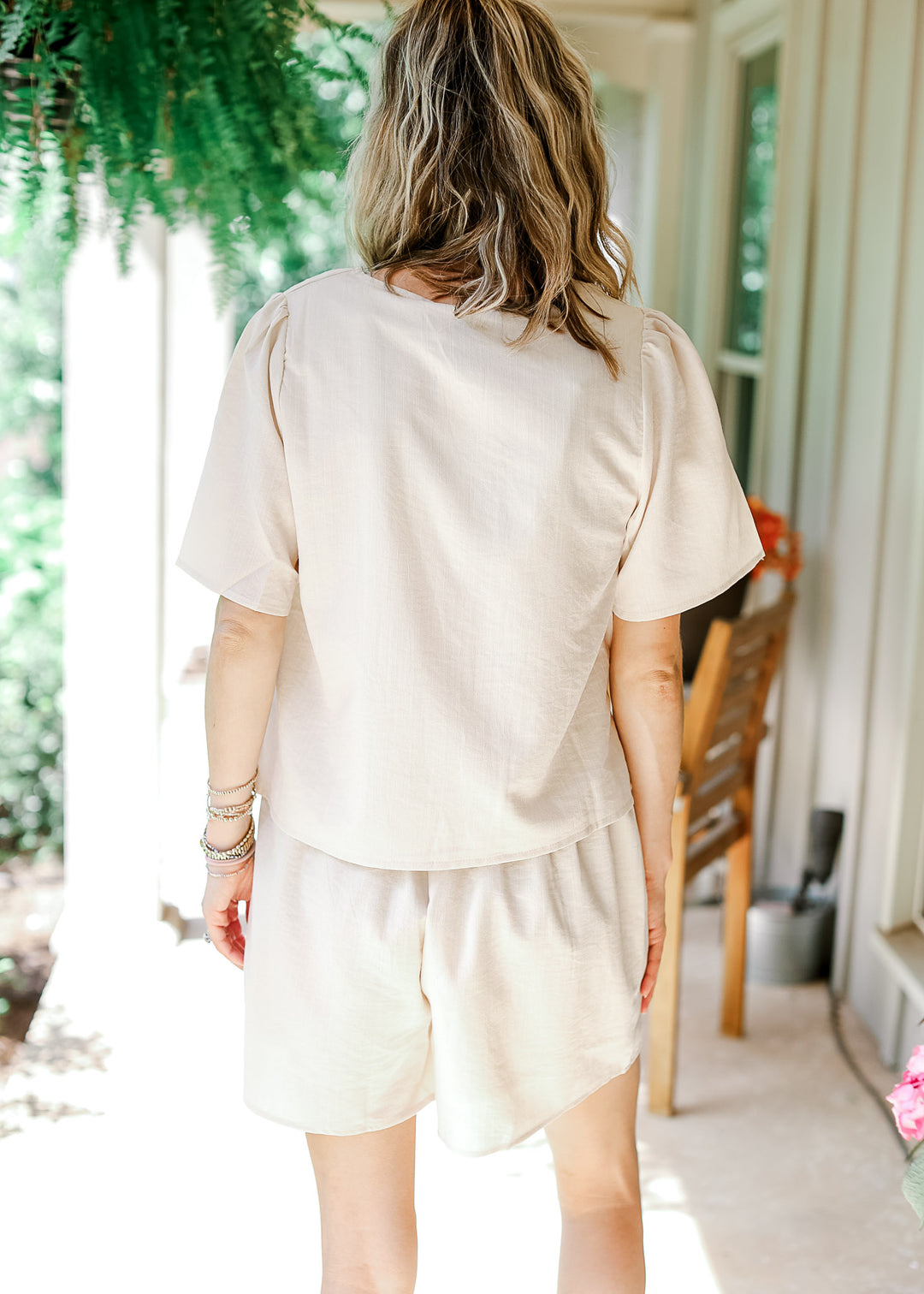 Model wearing a cream short set with pleated short sleeves and shorts with elastic waist. 