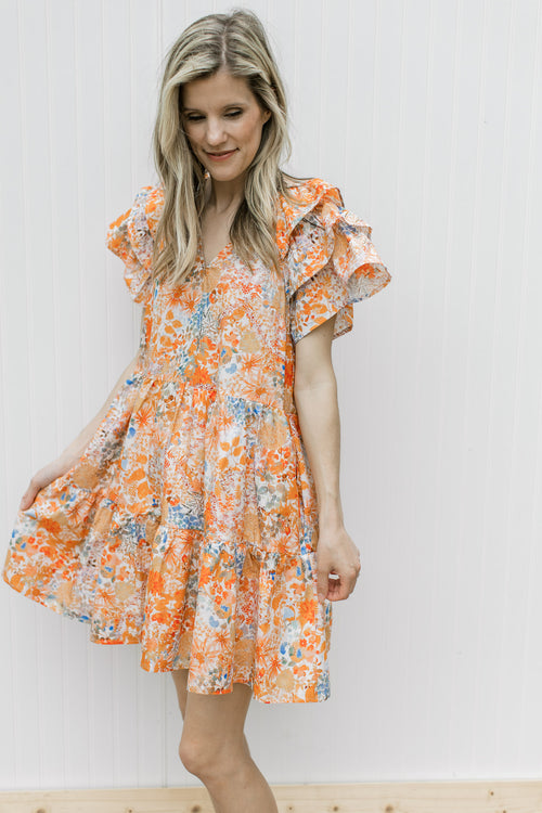 Model wearing a cream above the knee dress with orange and blue flowers and layered short sleeves.