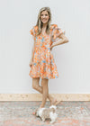 Model wearing sandals with a cream dress with orange and blue flowers and layered short sleeves.