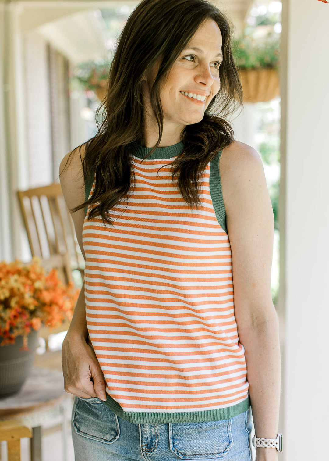 Model wearing a sleeveless orange and white striped top with olive trim at neck, arms, and hem.