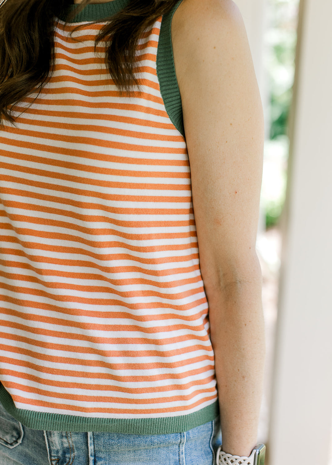 Close up of olive ribbed trim at arm, neck and hem of an orange and cream sleeveless top.