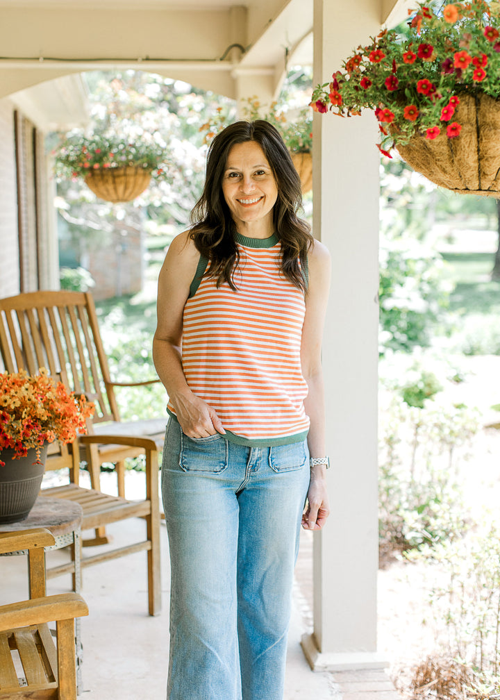 Model wearing jeans and an orange and white striped top with olive trim at neck, arms, and hem.