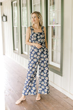 Model wearing a navy jumpsuit with white flowers, tank sleeves and wide legs.