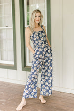 Model wearing a navy jumpsuit with white flowers, tank sleeves and button front.