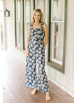 Model wearing a navy jumpsuit with white floral, tank sleeves and wide legs.