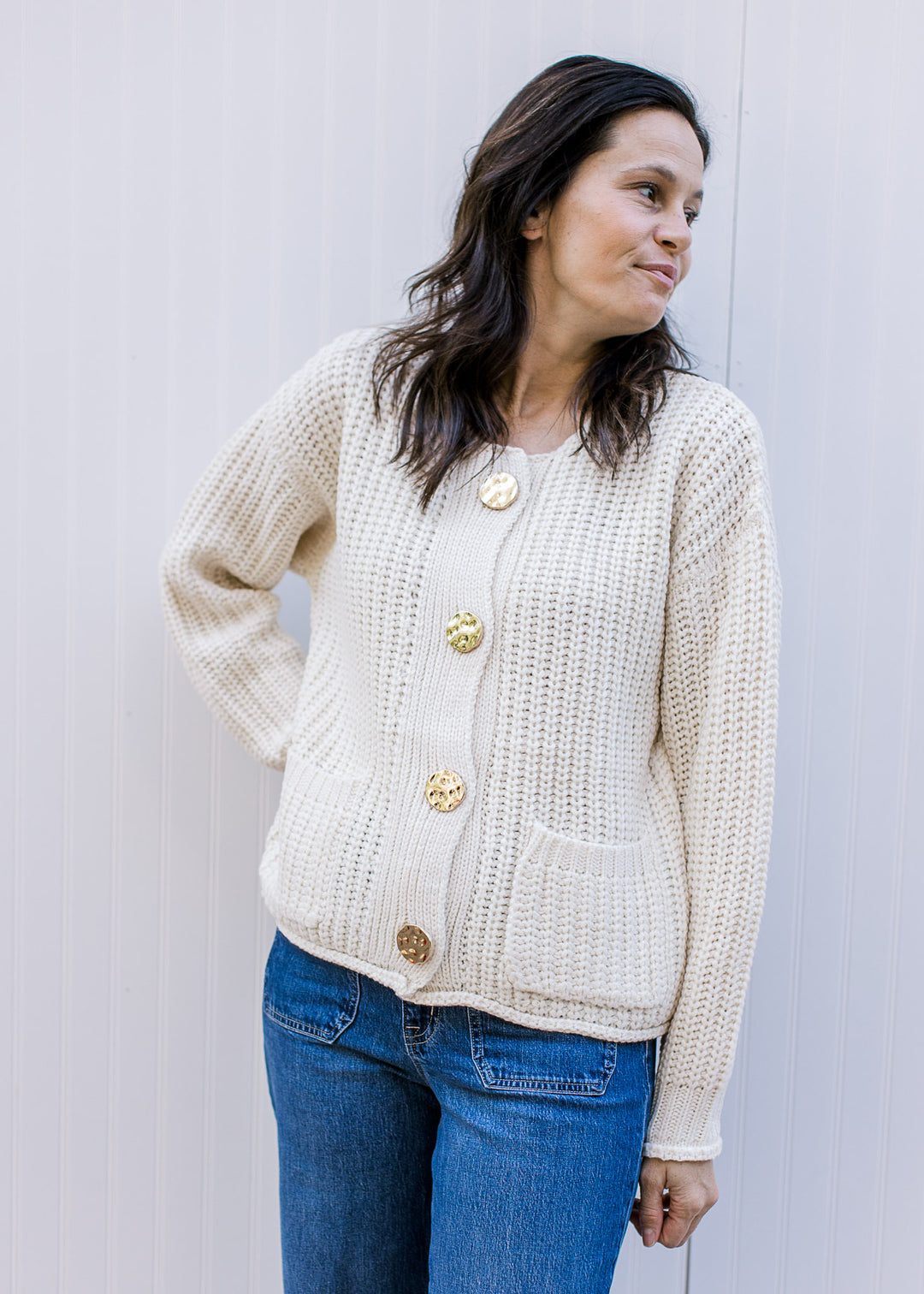 Model wearing a cream cable knit cardigan, with oversized gold buttons and round neck. 