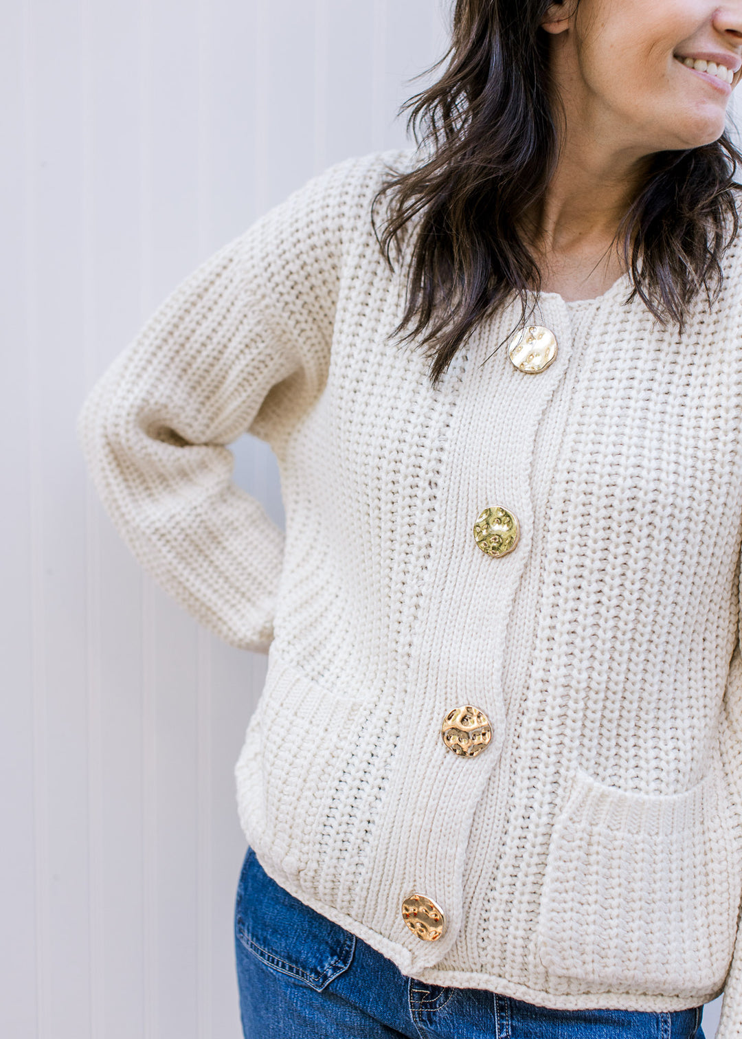 Model wearing a cream cable knit cardigan, with gold buttons and patch pockets. 