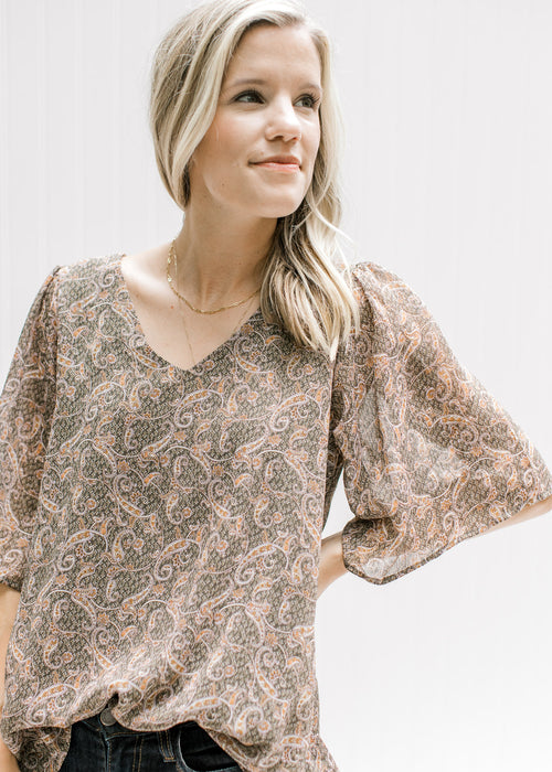 Model wearing a sage lined top with a tan paisley print, batwing sheer short sleeves and a v-neck. 