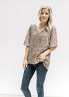 Model wearing jeans with a sage v-neck top with a tan paisley print and batwing sheer short sleeves.