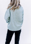Back view of Model wearing a pale blue sweater with a collar, long sleeves and a v-neck.