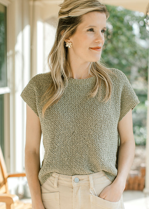 Model wearing a pale sage knit sweater with  capped sleeve and a round neck. 