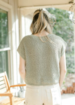 Back view of Model wearing a pale sage knit sweater with  capped sleeve and a round neck. 