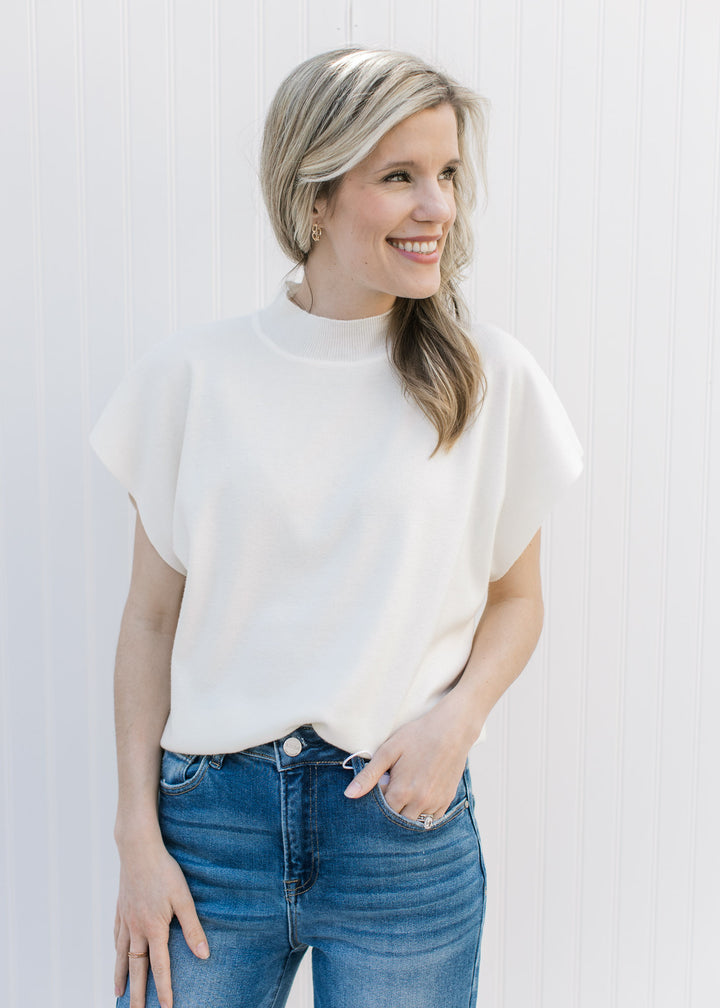 Model wearing a cream sweater with a mock neckline, extended cap sleeve and slightly cropped fit. 