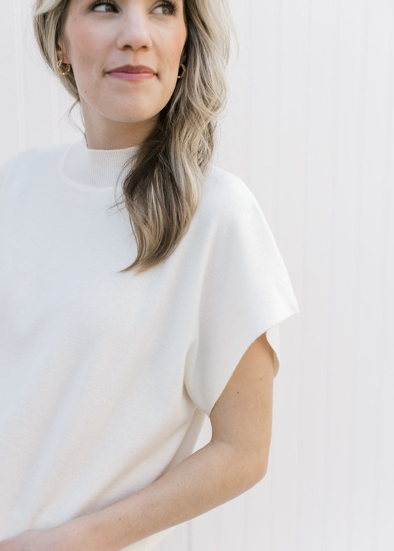 Close up of mock neck and extended cap sleeve on a cream sweater with a cropped fit. 