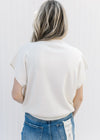 Back view of Model wearing a cream sweater with a mock neckline and extended cap sleeve.