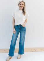Model wearing jeans with a cream sweater with a mock neck, extended cap sleeve and cropped fit.