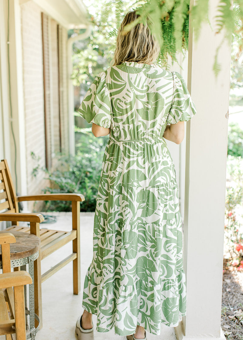 Back view of Model wearing a cream dress with green palm leaves and bubble short sleeves. 