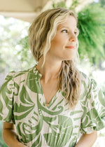 Close up of v-neck on a cream dress with green palm leaves and an elastic waist. 