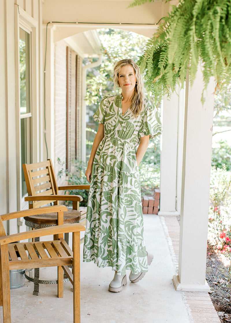 Model wearing a cream dress with green palm leaves, elastic waist and pockets. 