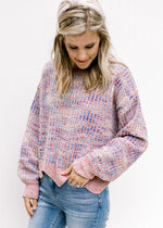 Model wearing a lilac striped sweater with an abstract background, long sleeves and a wavy hem. 