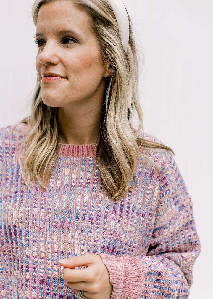 Close up of lilac stripes on an abstract blue, cream and purple background of a long sleeve sweater.