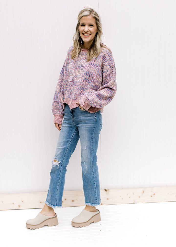 Model wearing jeans, mules and a lilac striped sweater with an abstract background and a wavy hem. 