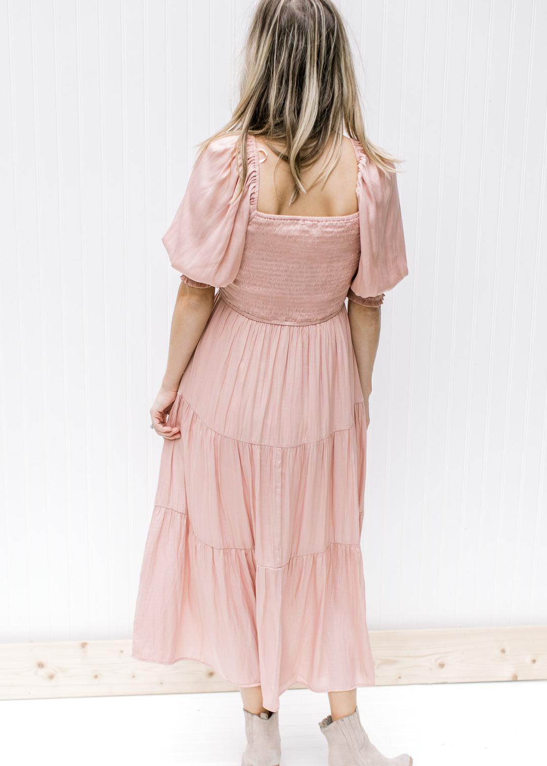 Back view of Model wearing a blush colored midi dress with a smocked bodice short sleeves.  