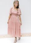 Model wearing a blush, v-neck  midi dress with a smocked bodice and bubble short sleeves.  