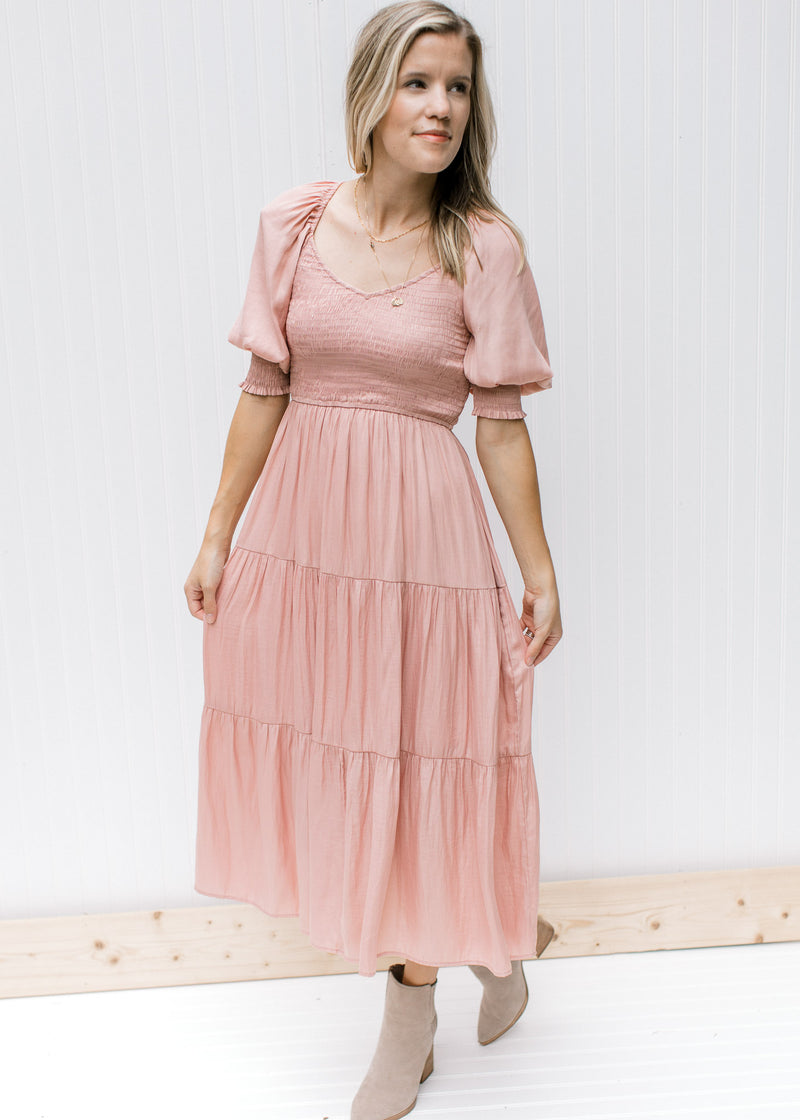 Model wearing a blush, v-neck  midi dress with a smocked bodice and bubble short sleeves.  