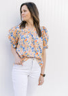 Model wearing a peach top with a floral pattern, v-neck and bubble short sleeves. 