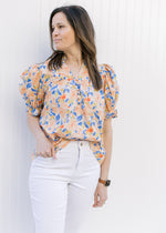 Model wearing a peach top with a floral pattern, v-neck and bubble short sleeves. 